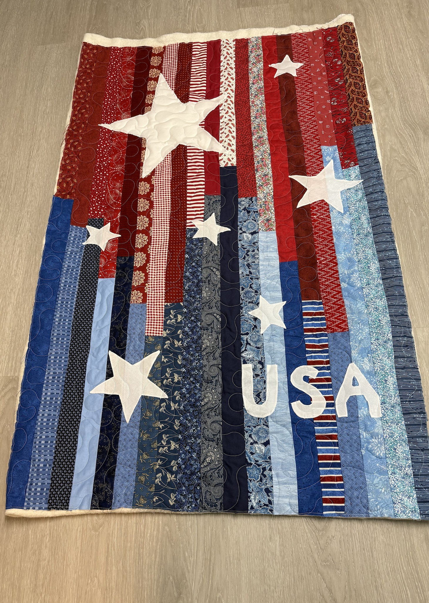 Patriotic quilt with white appliqued stars and USA lettering, pieced by JoAnne Scafidi and quilted by Lady Bird Quilts