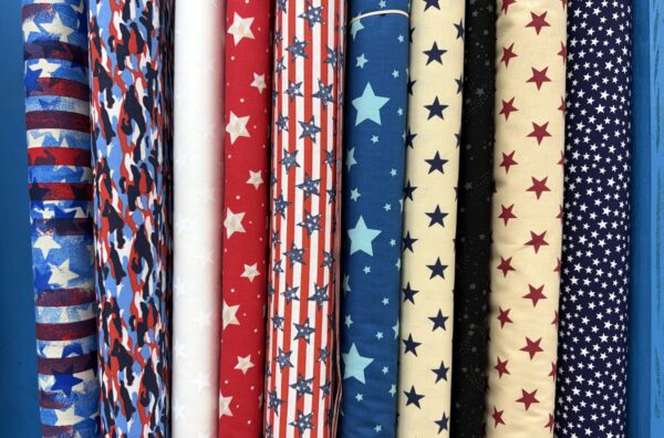Assorted patriotic stars and stripes cotton fabric bolts on the shelf at Lady Bird Quilts