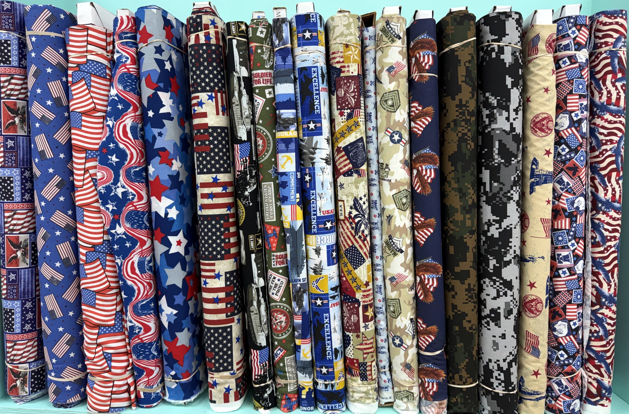 Military branch and camo print cotton fabric bolts including Army, Navy, Air Force, and Marines prints at Lady Bird Quilts