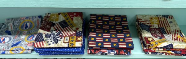 Folded patriotic and military print cotton fat quarters on the shelf at Lady Bird Quilts